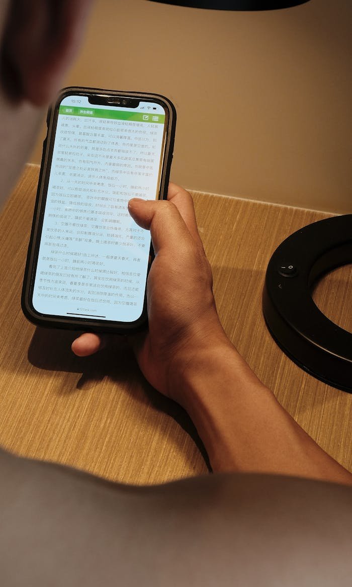A person holding a smartphone, reading content indoors with focused light.