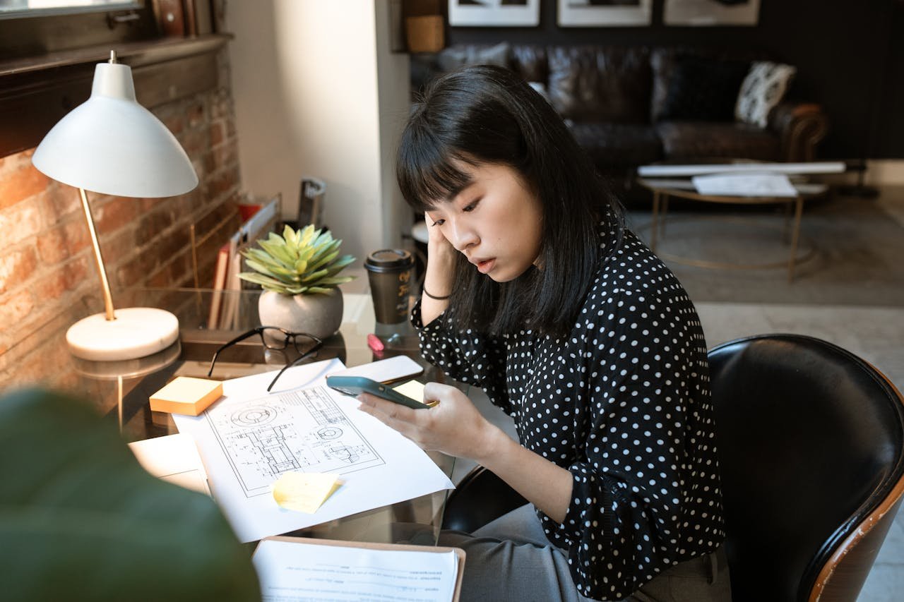 Young woman engrossed in smartphone work at a cozy office desk.